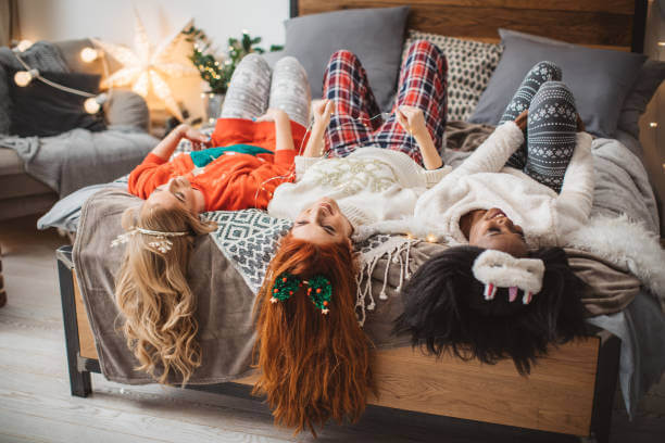 Three young women having Christmas eve pajama party at home. They make jokes and laughing while laying  in bed
